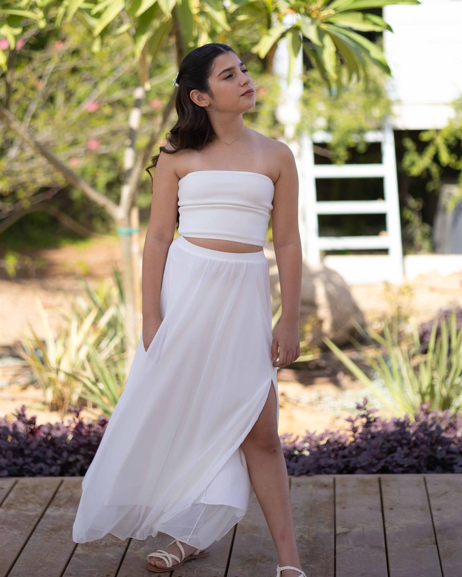 Young girl in a white dress photographed outdoors for a milestone portrait.